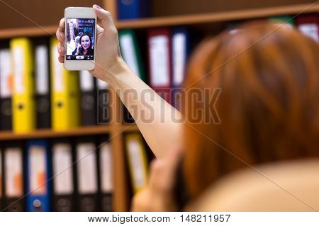 Businesswoman holding landline telephone taking Self Portrait on Mobile Phone Camera with Office colroful Folders on Background