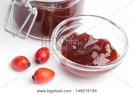 Rose hip jam and fruits from above over white, also rose haw or rose hep. Marmelade in glass jar and bowl. Shells of red fruits can be eaten raw and are one of the richest vitamin C sources in plants.