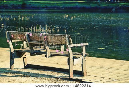 Rustic wooden park bench draped in faded pink party decorations on the bank of an emerald green river. Audley, Royal National Park, Australia