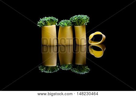 A group of three broccoli embedded into pasta manicotti on a black reflection backround