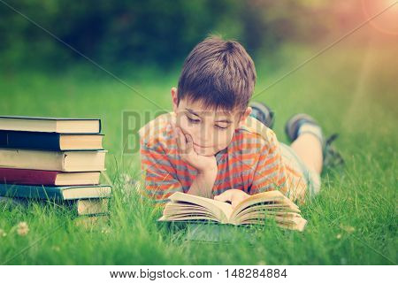 seven years old child reading a book lying on the grass