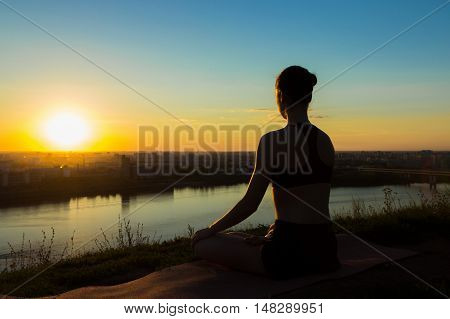 Sporty woman in lotus position in the park at sunset. Sunset light, golden hour, lens flares. Freedom, health and yoga concept.