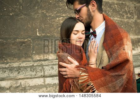 Young fashion elegant stylish couple standing, embracing, wrarps in pled on streets of old european city