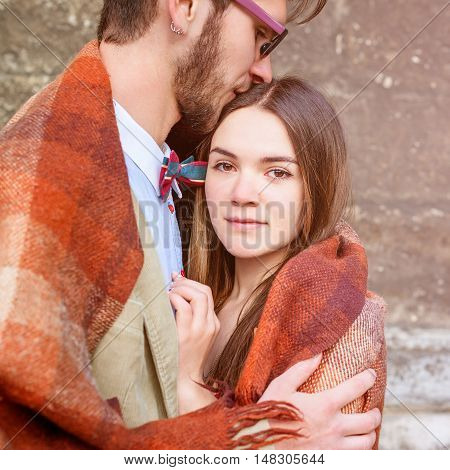 Young fashion elegant stylish couple standing, embracing, wrarps in pled on streets of old european city