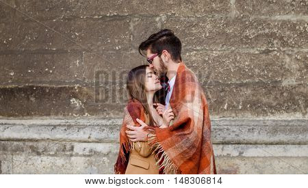 Young fashion elegant stylish couple standing, embracing, wrarps in pled on streets of old european city