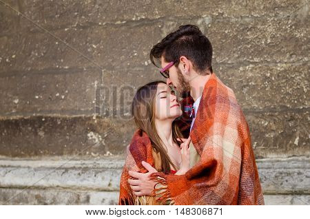 Young fashion elegant stylish couple standing, embracing, wrarps in pled on streets of old european city