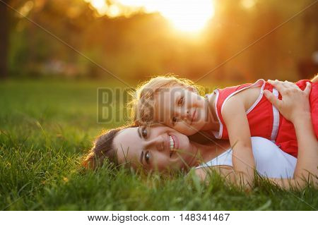 Mother and daughter lying on the lawn. Family in the city park outdoors. Happiness of motherhood and childhood.