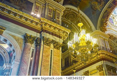 SAINT PETERSBURG RUSSIA - APRIL 25 2015: The massive chandelier and richly decorated walls of St Isaac's Cathedral with stone painted carved and gilt elements on April 25 in Saint Petersburg.