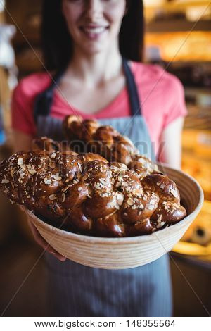 Mid-section of female baker holding freshly baked loaf of bread in bakery shop