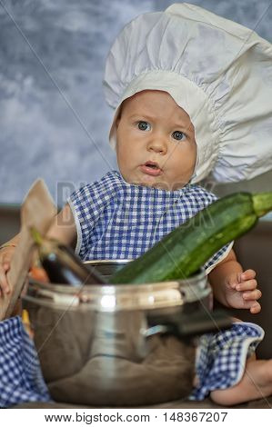little child dressed as a chef plays with vegetabeles