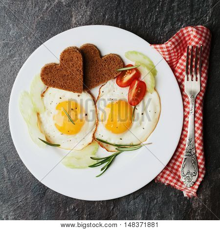 Fried eggs with fresh vegetables and toast in shape of heart on white plate. Delicious breakfast for showing warm feelings.