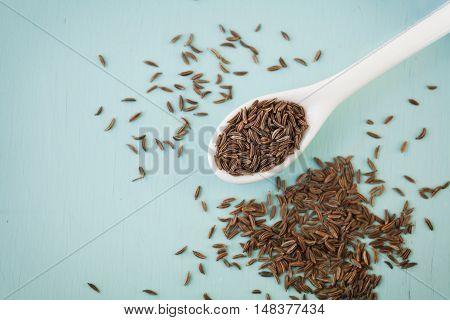 Cumin seeds or caraway in white spoon on wooden board.