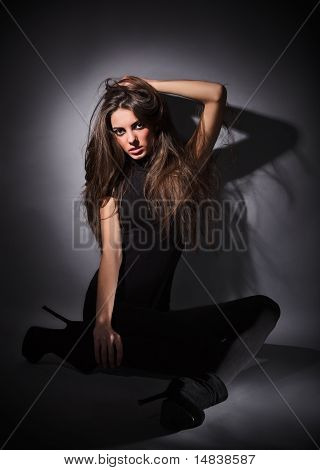 Mladý štíhlý Glamour Lady s dlouhými vousy, oblečený v černých šatech Combi sedí na podlaze, tmavě klíč