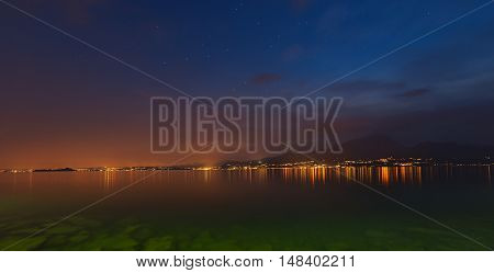 Lago di Garda at night (Garda Lake) the largest Italian lake of glacial origin with the lights of the coast of Lombardy and starry sky Italy