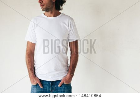 Man wearing blanc t-shirt posing against white wall, toned photo, front tshirt mockup on model