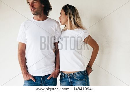 Two models man and woman wearing blanc t-shirt posing against white wall, toned photo, front tshirt mockup for couple