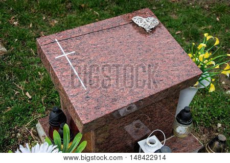 Urn grave with cross on traditional cemetery. Votive candles lantern and flowers on tomb stones in graveyard. All Saints' Day. All Souls' Day. Gravestones in village Tvrdomestice, Slovakia