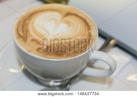 White cup of cappuccino with heart pattern on the whipped milk foam