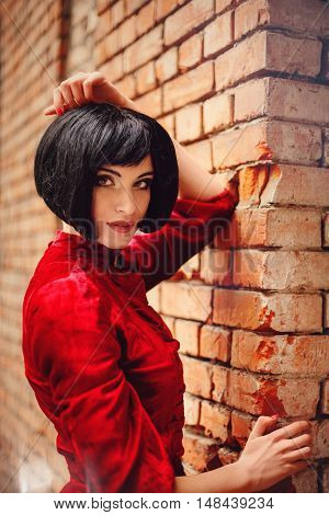 Young brunette girl in vintage romantic red dress near the old brick wall. Fairy tale nostalgic mood. Warm tinted