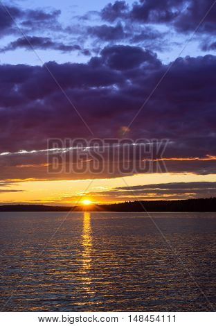 Vyborg. Bright summer sunset over Gulf of Vyborg. Evening calm in sea Bay Leningrad region Saint-Petersburg Russia. Sun disappears behind the forest and reflected in water and clouds
