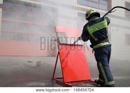 Firefighter with hose directs water on red shield. Inscription on the uniform Fire protection MES of Russia.