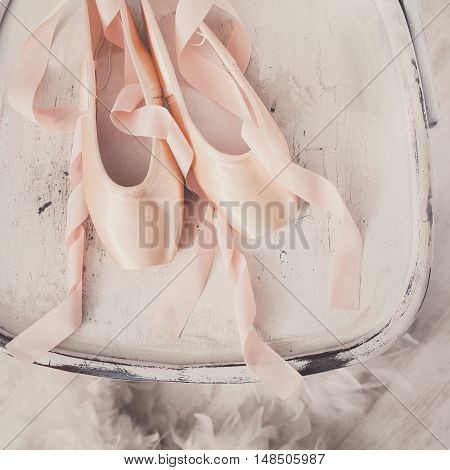 Pastel pink ballet shoes background. New pointe shoes with satin ribbon lay on white rustic shubby chic chair near feather boa, top view from above