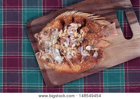 Deep fried fish ,Nile tiapia, with crispy garlic on butcher served. Top view.