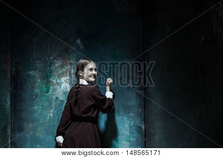 Halloween theme: Portrait of a young smiling girl in school uniform as killer woman against school board . The image in the style of Halloween and Addams family