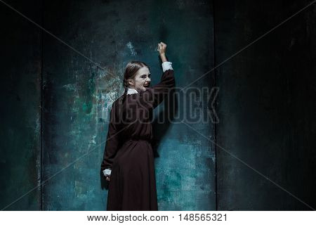 Halloween theme: Portrait of a young smiling girl in school uniform as killer woman against school board . The image in the style of Halloween and Addams family