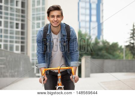 A guy in a blue denim jacket on orange bicycle. Man on the background of the city with a backpack on a bike