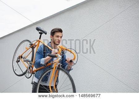 Guy in denim jacket going down the stairs holding an orange bicycle. Student with the bike going down