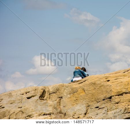 Mother and daughter sit on top of the mountain against the blue sky with white clouds