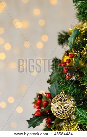 Festive Christmas close up of tree decorated with gold baubles tinsel and holly berries. Bokeh background copy space. Vertical.