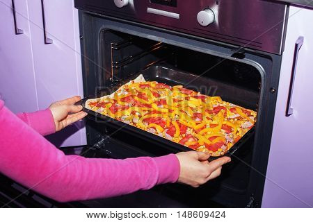 The woman pushed the pizza in the oven. The concept of cooking.