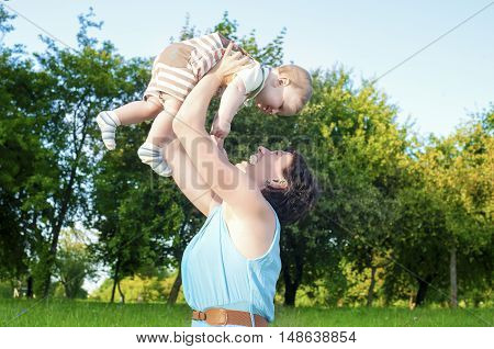 Happy Mother Tossing Up Her Kid While Playing with Him in Park Outdoors. Horizontal Image