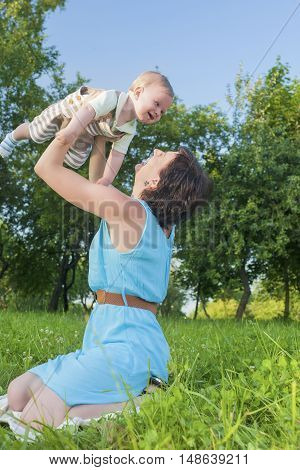 Happy Mother Tossing Up Her Kid While Playing with Him in Park Outdoors. Vertical Image