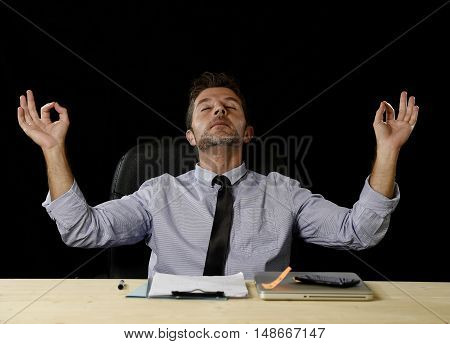 young attractive happy businessman relaxing with hands in yoga position cheerful and friendly wearing shirt and tie isolated in black background sitting at office desk chair in relax at work concept