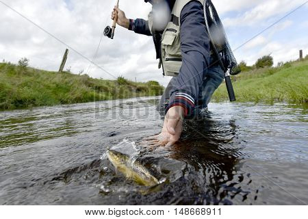 Fly-fisherman catching brown trout in river