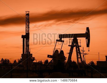 Oil rig and derrick silhouette during sunset in the oilfield. Oil and gas concept. Toned.