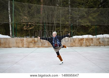 Young girl skating on one leg with arms outstretched to the sides on a skating rink