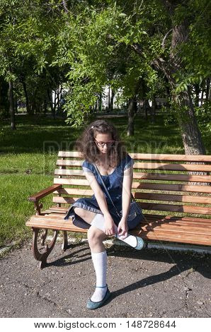 The girl in the blue dress dress shoes on a wooden bench in the park