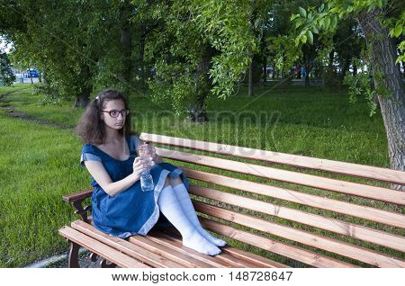 A girl sits on a park bench with a bottle of water