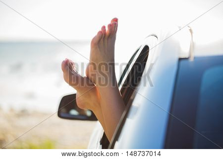 summer vacation, holidays, travel, road trip and people concept - close up of young woman feet showing from car window