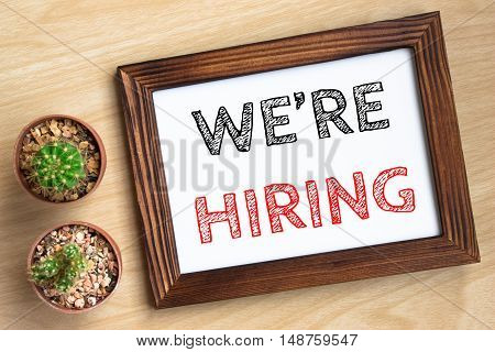we're hiring, text message on wood frame board on wood table / business concept / Top view