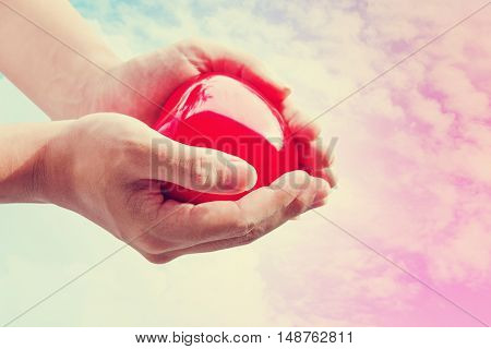 Hand holding red hart on colorful sky, vintage tone