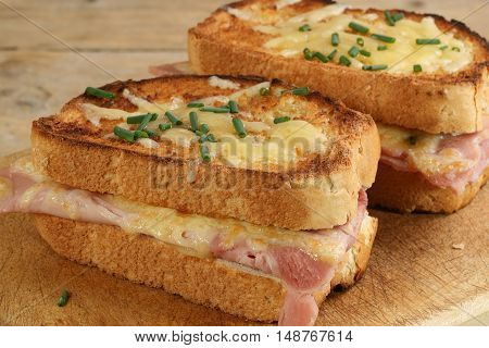 two slices of croque monsieur cheese and ham on a wooden board