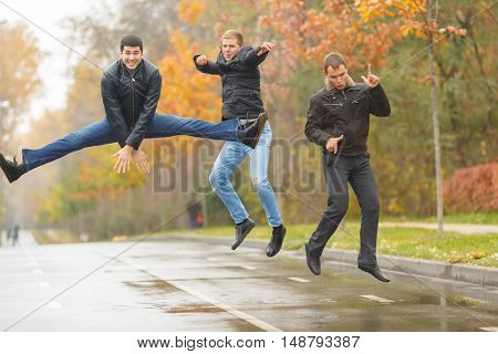 Three young men in black jackets jumping for merry-making in alley in park