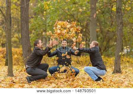Three men in black jackets hunker down and pop-up yellow maple leaves in park