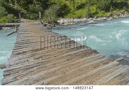 Old wooden bridge across mountain river. The Kucherla river Altai Mountains Russia. Sunny summer day.