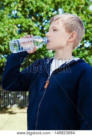 Young teenage boy drinking healthy still water in park summer time